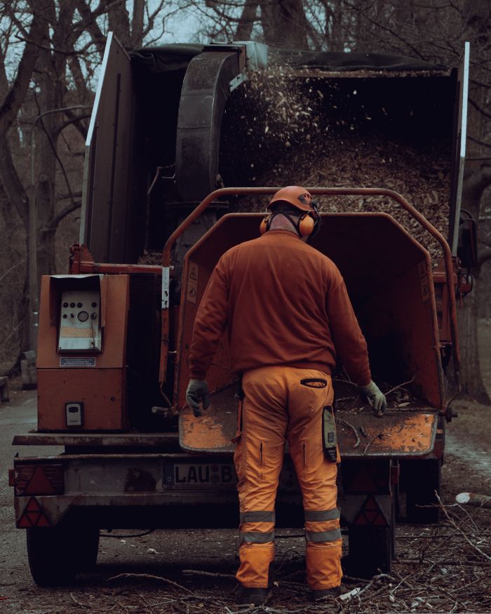 about-04 Adult male worker using a wood chipper in an outdoor forest setting.