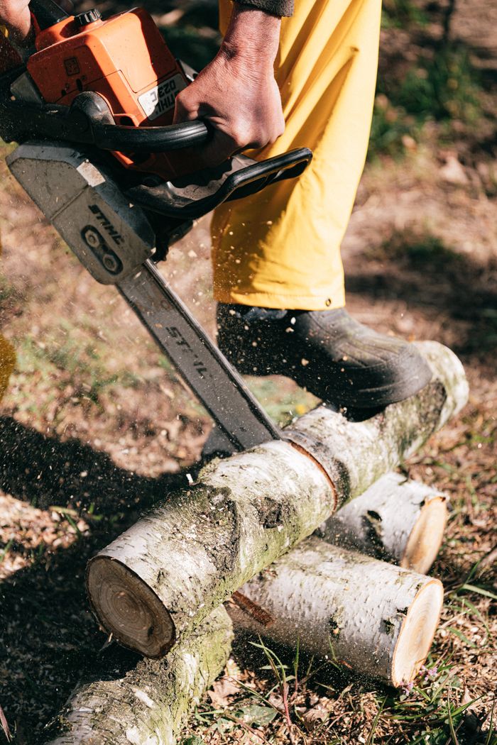 about-03 A person using a chainsaw to cut wooden logs outdoors, showcasing forestry work.